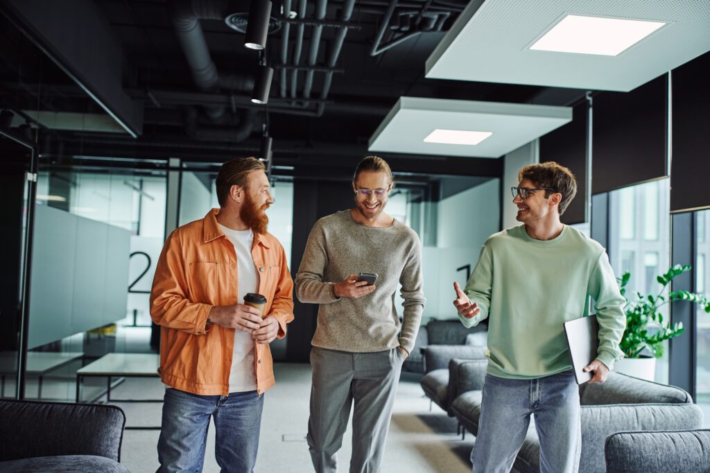 smiling entrepreneur in eyeglasses holding laptop and discussing startup with partners, walking